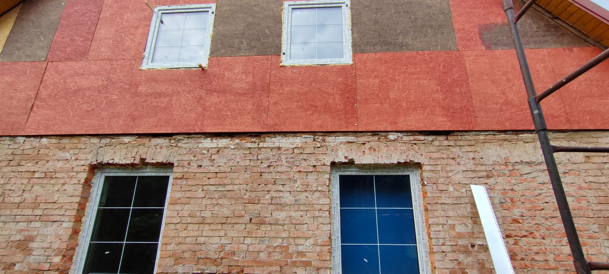 Fragment ściany domu z częściowo wykonanym ociepleniem: widoczna stara cegła, nowe okna i płyty OSB przygotowane pod dalsze prace.