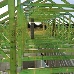 Firma Remontowo budowlana Łukasz Beyer - Konstrukcja dachu domu w trakcie budowy, impregnowane drewno w kolorze zielonym, widoczne metalowe łączniki i ściany z bloczków.