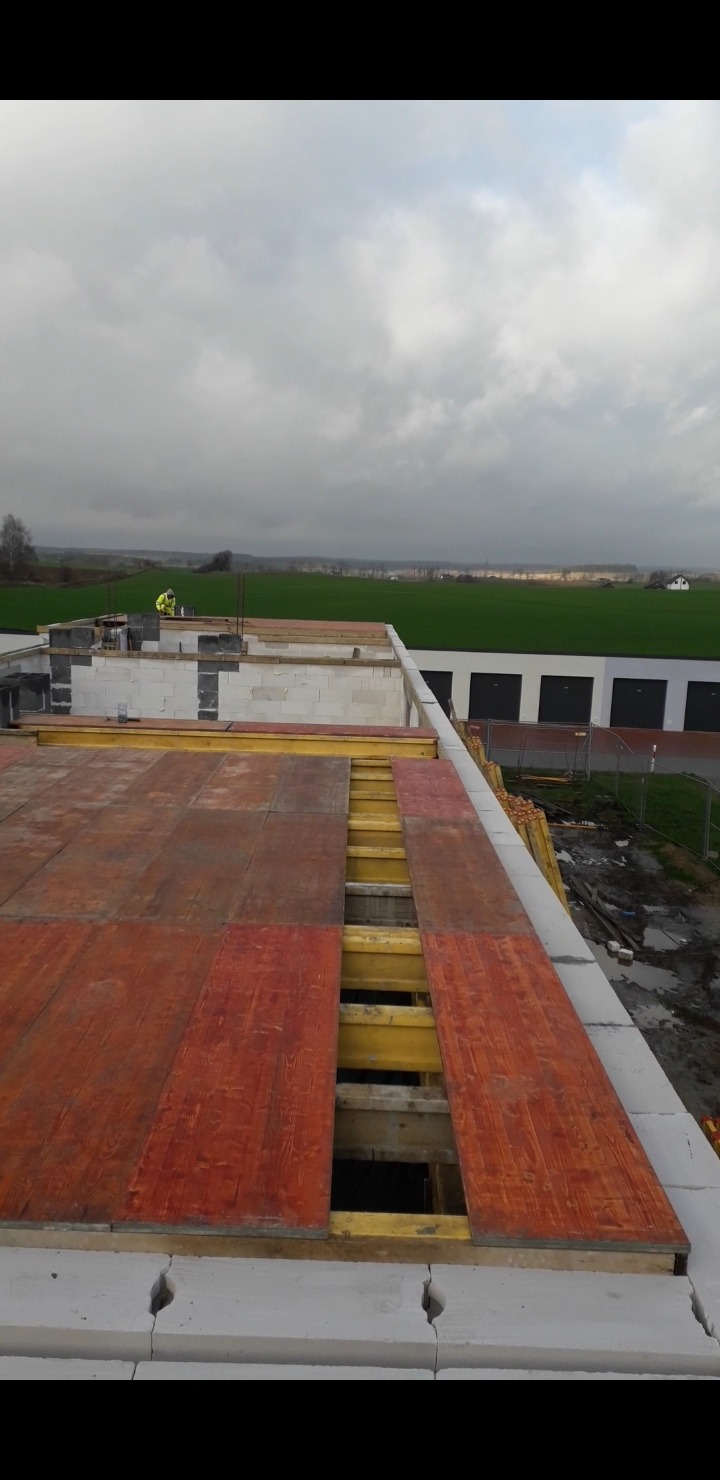 Budowa domu z pustaków ceramicznych Porotherm: widok z góry na strop z drewnianym szalunkiem, w tle zielone pole i pochmurne niebo.