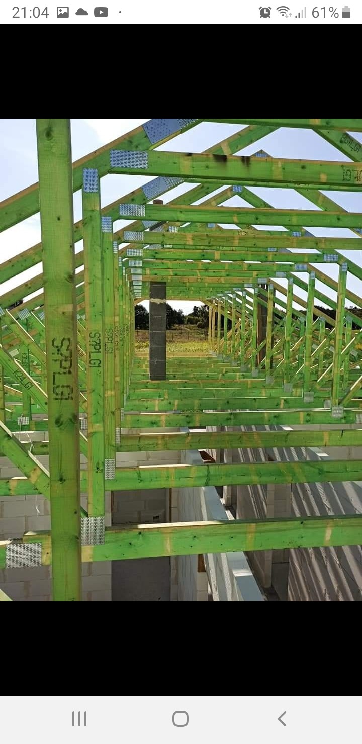 Konstrukcja dachu domu w trakcie budowy, impregnowane drewno w kolorze zielonym, widoczne metalowe łączniki i ściany z bloczków.