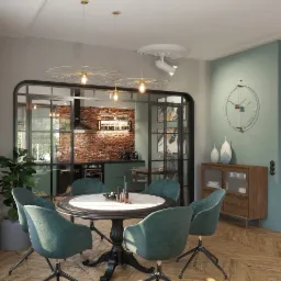 Wnętrze jadalni z okrągłym stołem, krzesłami obrotowymi w odcieniach zieleni, oświetleniem dekoracyjnym i widokiem na kuchnię z ceglaną ścianą.