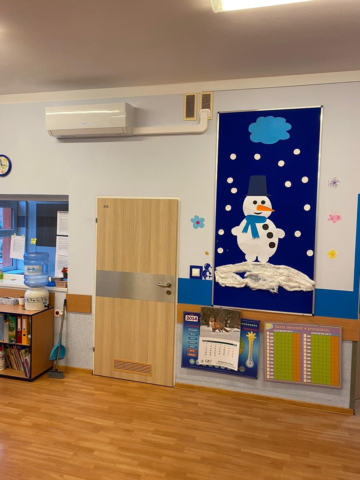 Klimatyzator ścienny zamontowany w przedszkolu w Warszawie, widoczne kratki wentylacyjne i dekoracja zimowa na ścianie.