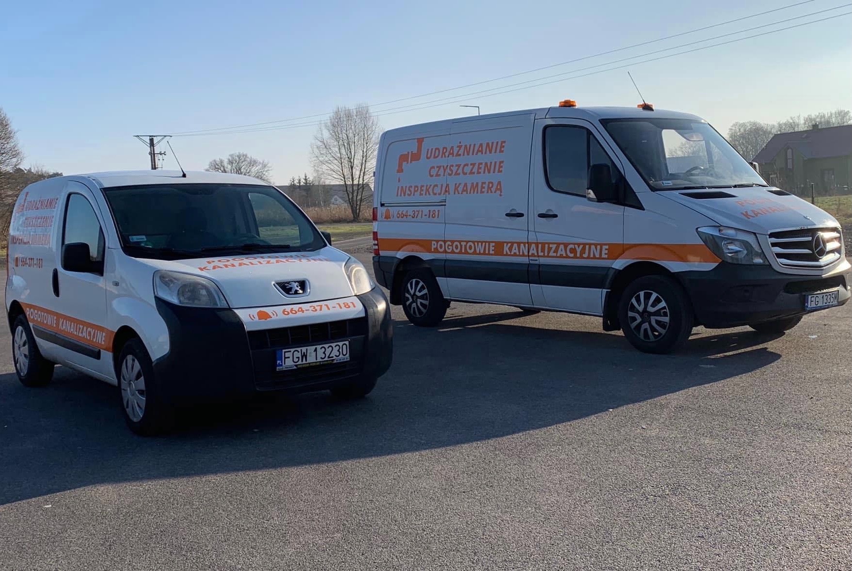 Dwa białe busy zaparkowane na asfalcie, z pomarańczowymi akcentami i napisami 'Pogotowie Kanalizacyjne' oraz numerem telefonu, w tle drzewa i budynki.