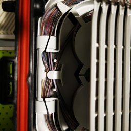 FiberOptic - Szczegółowe ujęcie rozdzielnicy światłowodowej z uporządkowanymi kablami w różnych kolorach, zainstalowanej przez firmę z Warszawy. Widoczne precyzyjne ułożenie przewodów wewnątrz obudowy.