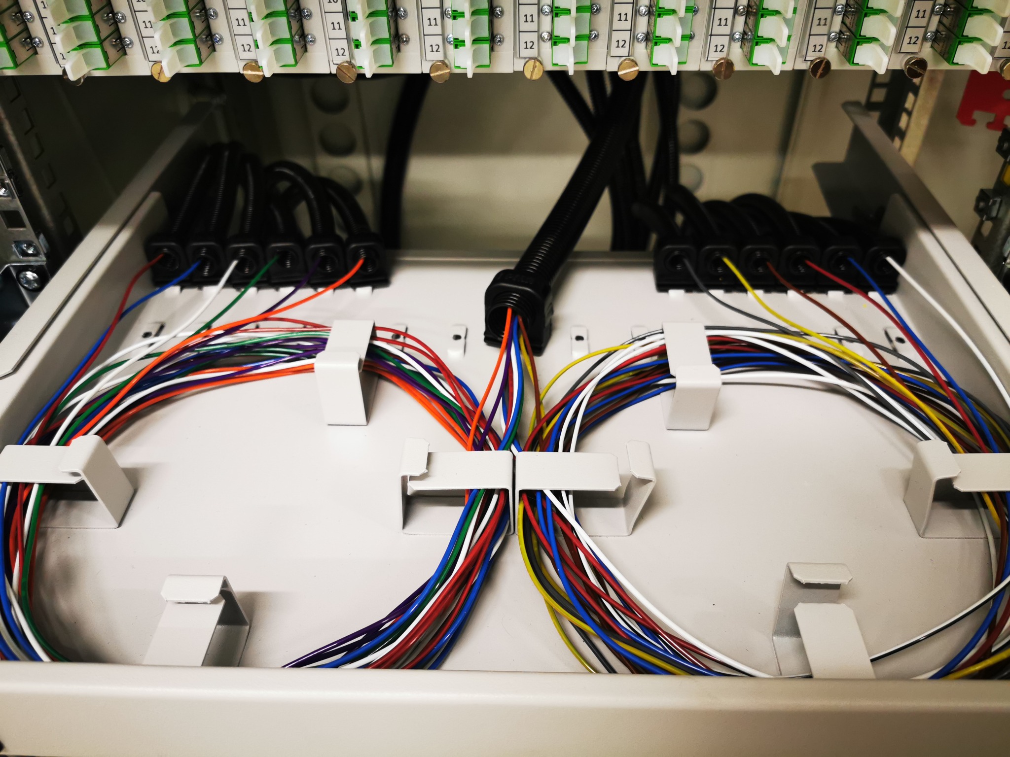 Panel krosowniczy z uporządkowanymi kablami światłowodowymi w różnych kolorach, widoczne złącza i oznaczenia numerów portów.