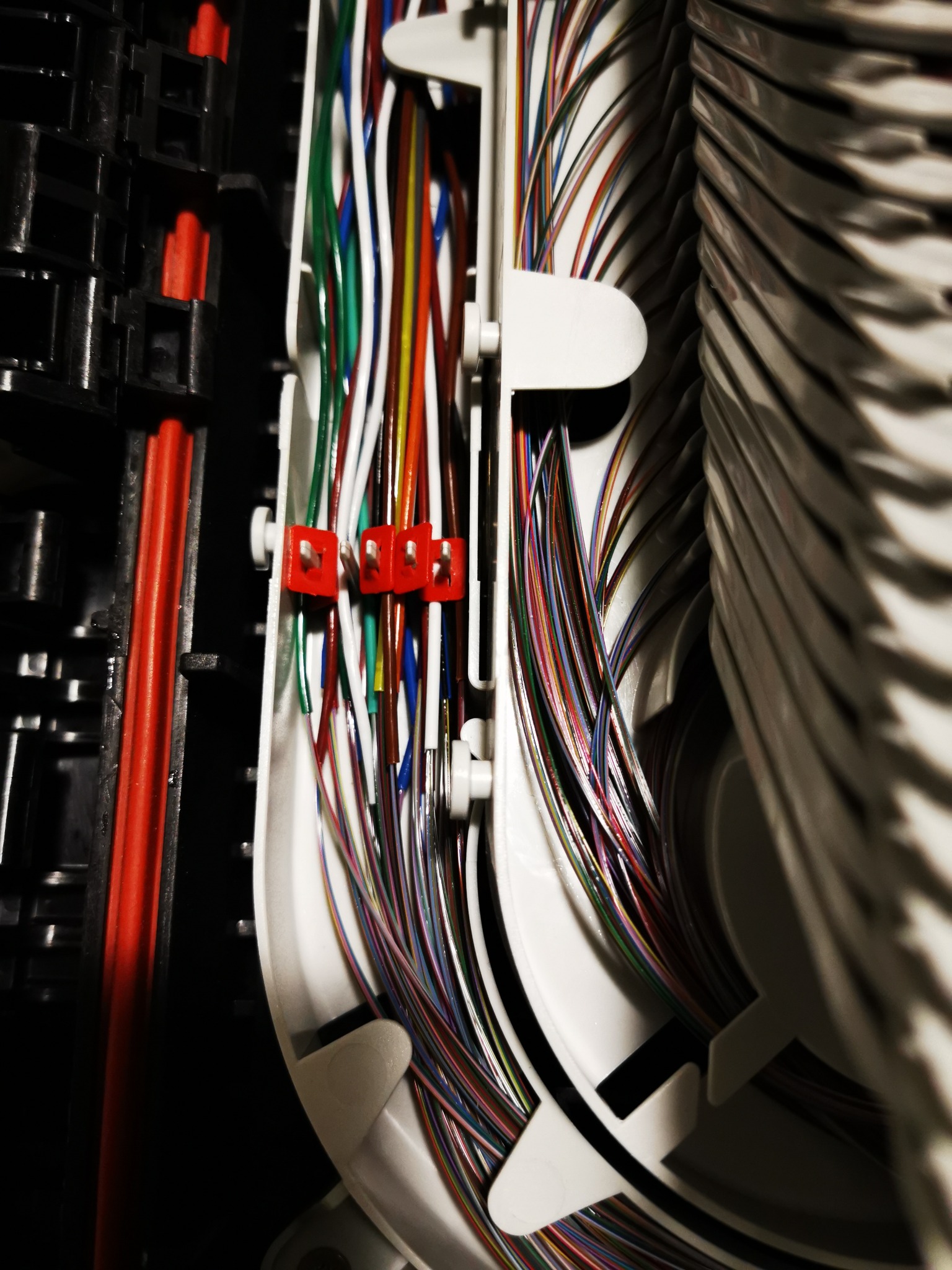 Szczegółowe ujęcie uporządkowanego panelu krosowniczego z kolorowymi kablami światłowodowymi, zabezpieczonymi białymi uchwytami, widoczne czerwone elementy mocujące po lewej stronie.