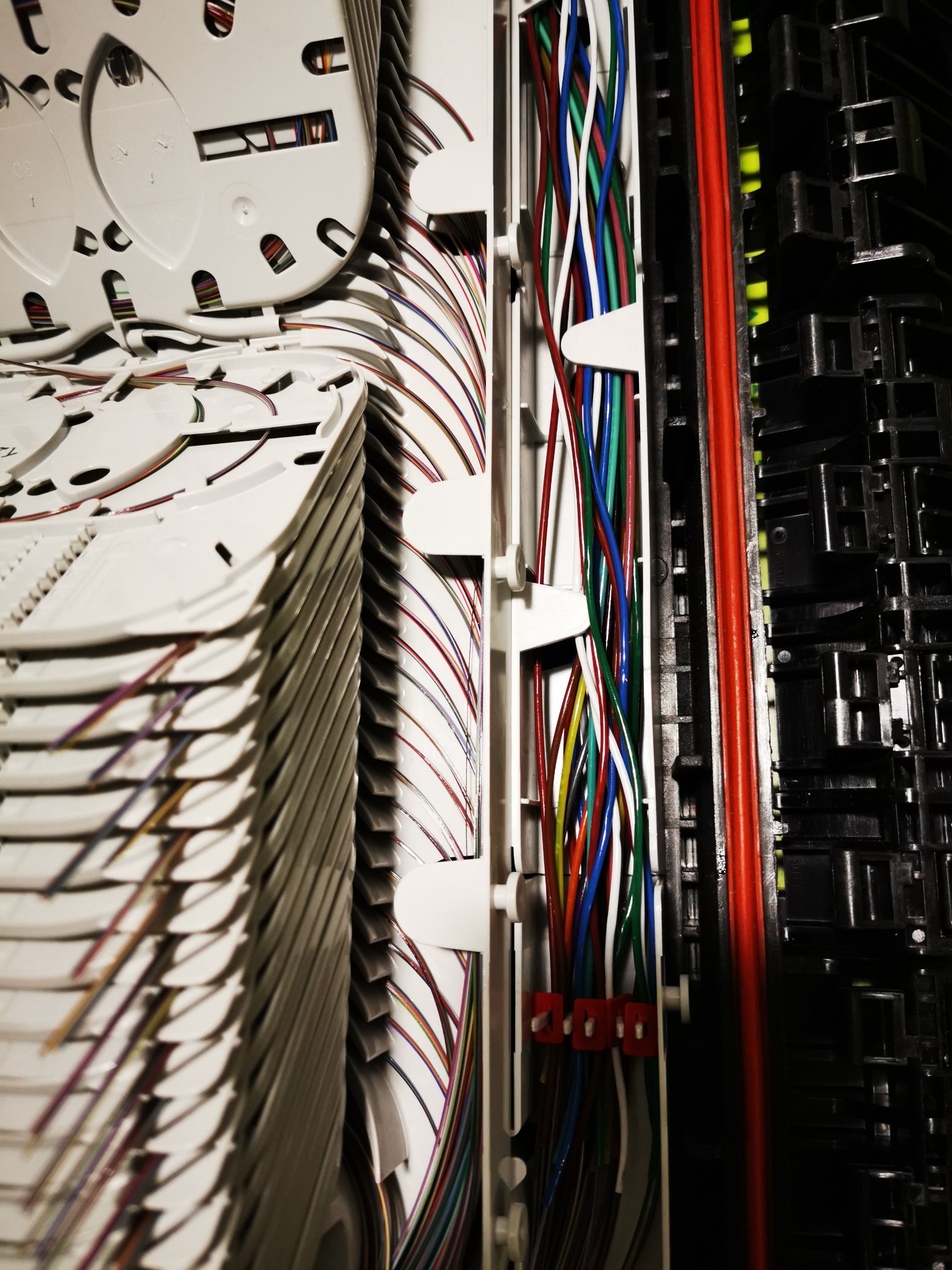 Szczegółowe ujęcie panelu krosowniczego z ułożonymi kablami światłowodowymi w kolorowych osłonkach, widoczne białe kasety i elementy mocujące przewody.