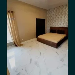 Jasna sypialnia z marmurową podłogą, beżowymi ścianami, dekoracyjną ścianą z trójwymiarowych paneli i ciemnobrązowym łóżkiem, oświetlona lampą sufitową.