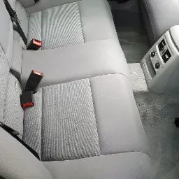 Wnętrze samochodu, tylna kanapa z szarej tapicerki, widoczne pasy bezpieczeństwa i nawiewy klimatyzacji.