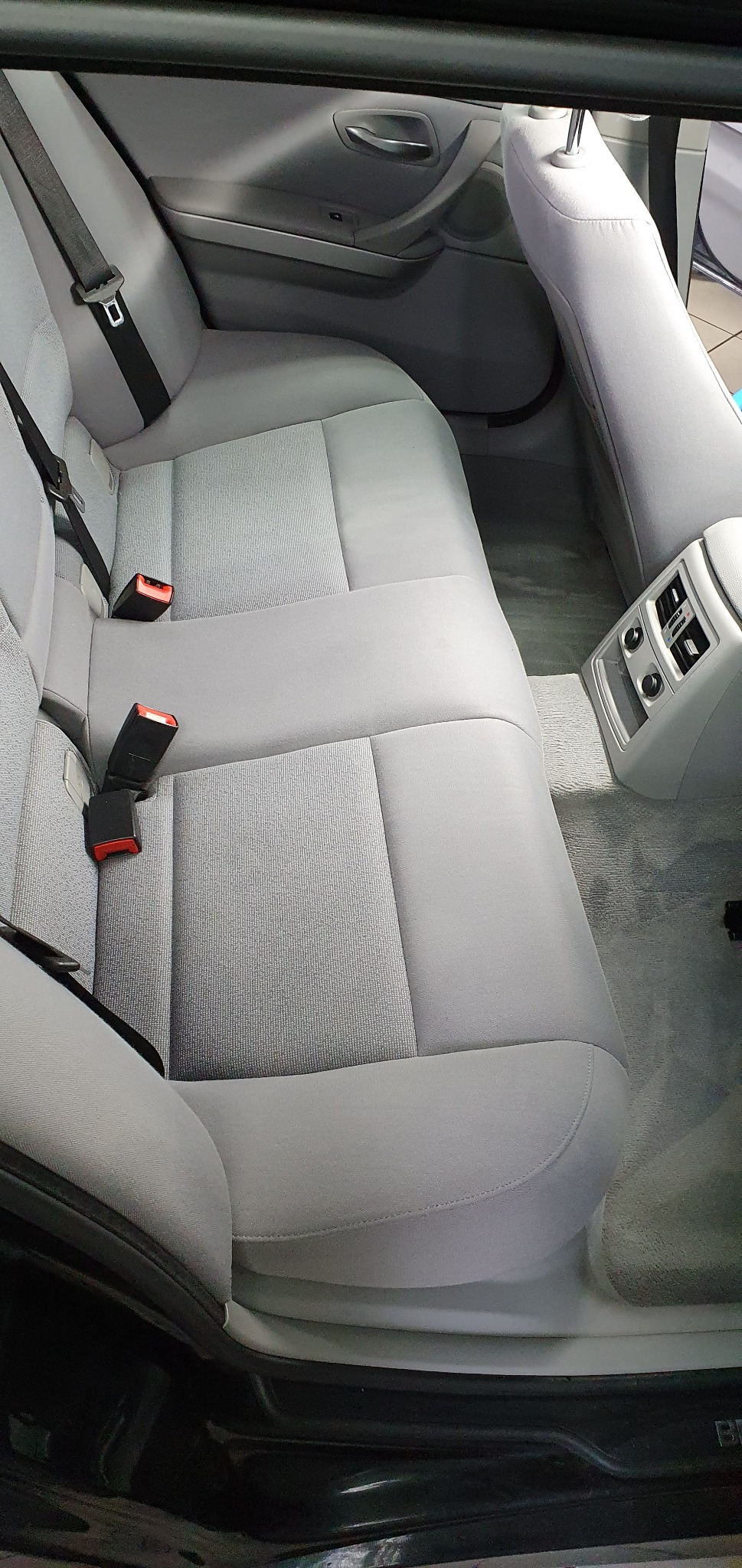 Wnętrze samochodu, tylna kanapa z szarej tapicerki, widoczne pasy bezpieczeństwa i nawiewy klimatyzacji.