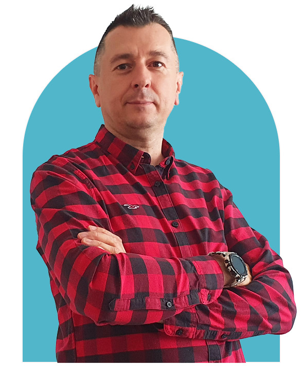 Portret mężczyzny z Rzeszowa w czerwono-czarnej koszuli w kratę, z założonymi rękami i zegarkiem na nadgarstku, na jasnoniebieskim tle.