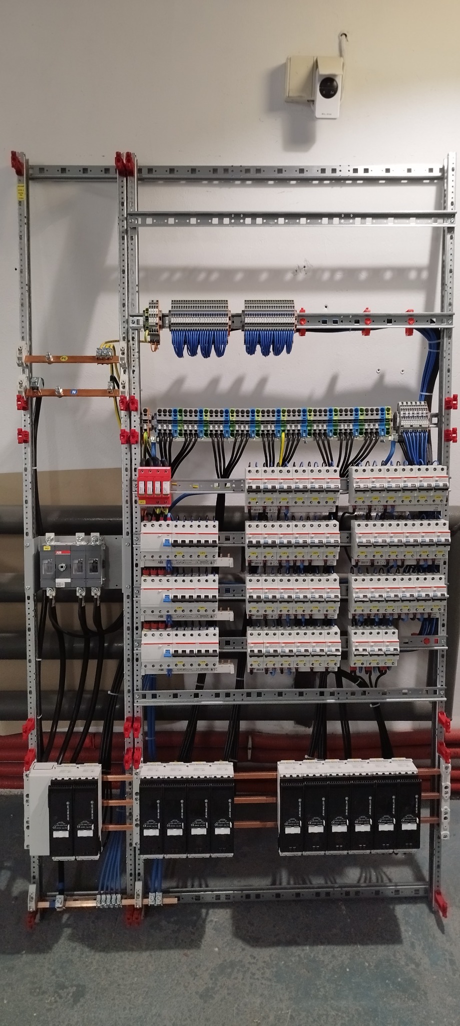 Rozdzielnica elektryczna w metalowej ramie z licznymi zabezpieczeniami i przewodami, zamontowana w pomieszczeniu w Czańcu. Widoczny również system mocowań i elementy instalacji.