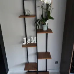 Metalowy regał z drewnianymi p&oacute;łkami w stylu loft, na kt&oacute;rym znajdują się białe ozdoby i doniczka z orchideą.