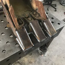 Wzmocnienie łyżki koparki poprzez dospawanie nowych zębów na stole spawalniczym, widoczne ślady spawania.