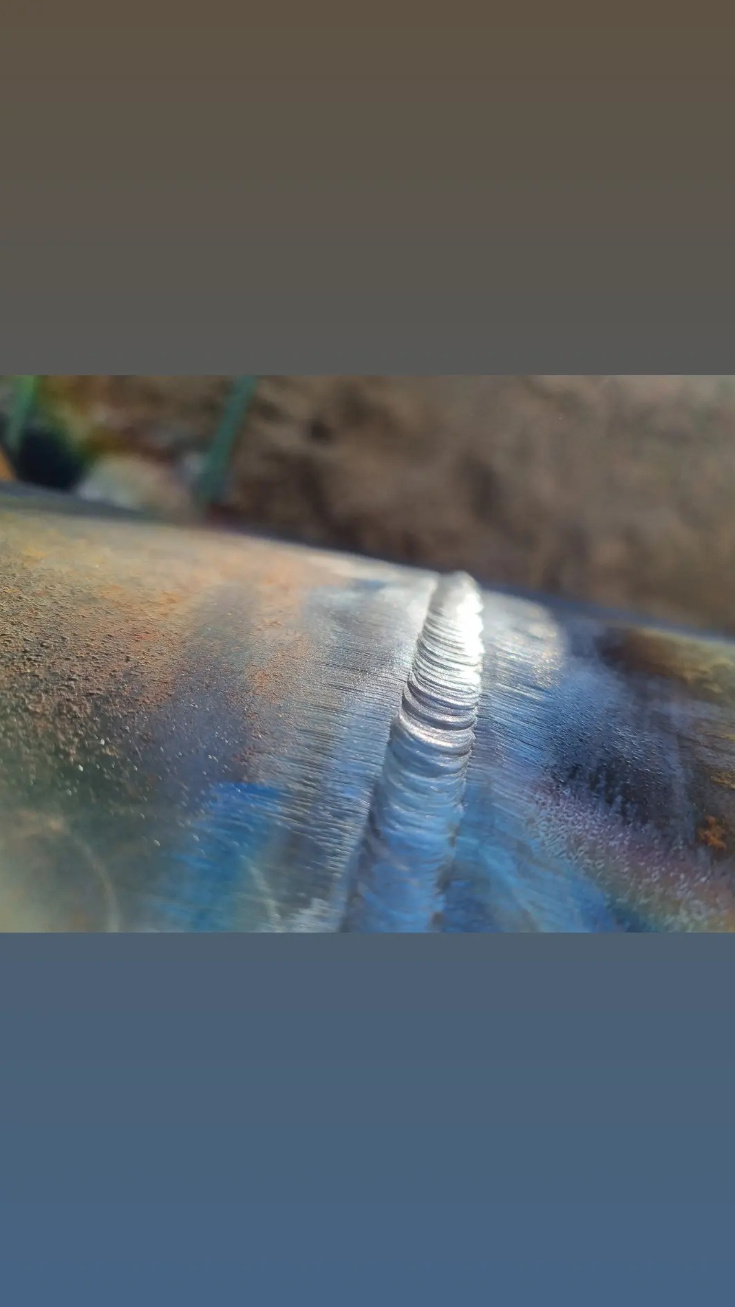 Zbliżenie na świeżo wykonany spaw na metalowej rurze, widoczne drobne nierówności i przebarwienia termiczne.