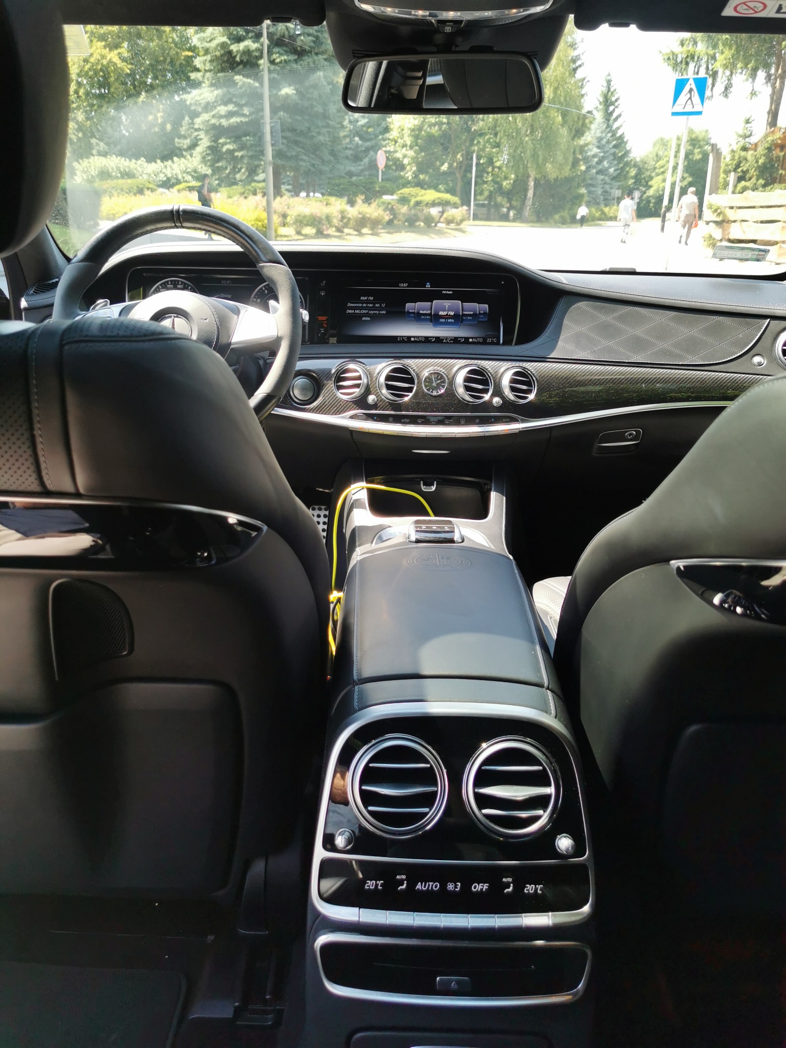 Wnętrze luksusowego samochodu Mercedes S Klasa AMG 63S, widok z tylnych siedzeń na deskę rozdzielczą i przednią szybę z widokiem na ulicę i przechodniów.