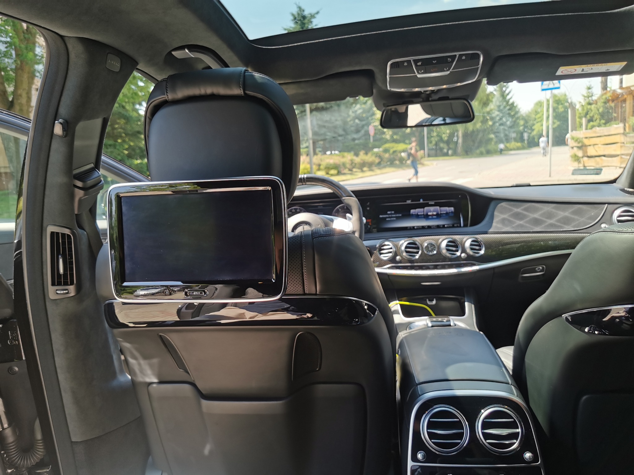 Wnętrze luksusowego samochodu Mercedes S klasa AMG 63S z panoramicznym dachem, widok z tylnego siedzenia na deskę rozdzielczą i ulicę.