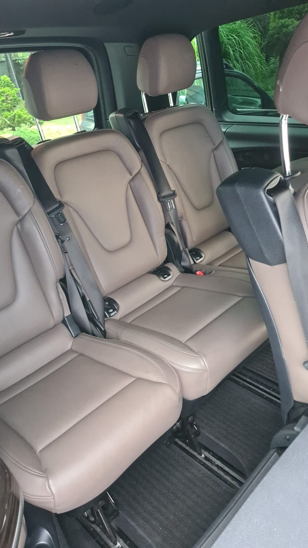 Wnętrze busa z trzema rzędami skórzanych, beżowych siedzeń z zamontowanymi pasami bezpieczeństwa, widok z perspektywy pasażera.