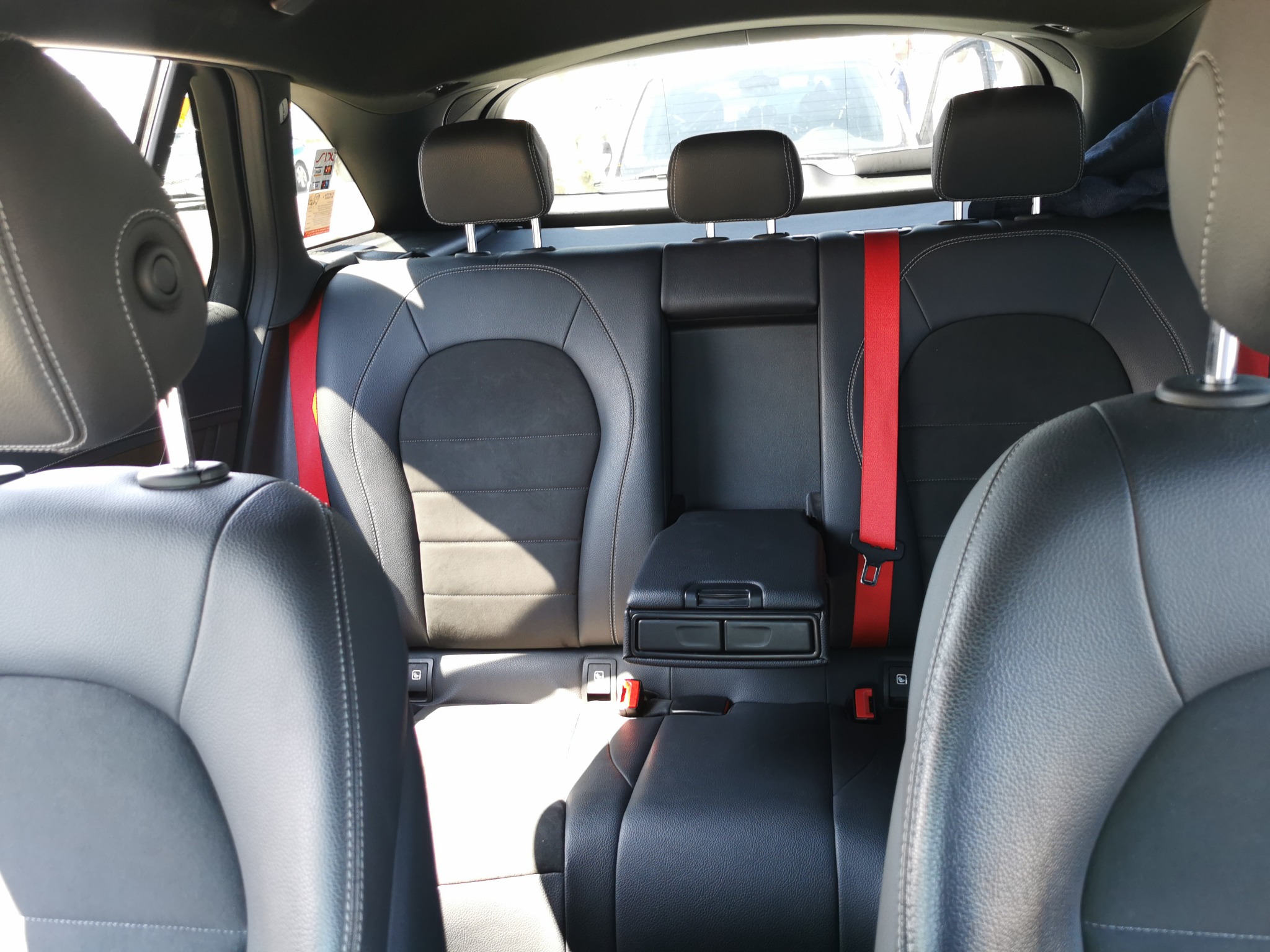 Wnętrze samochodu Mercedes GLC 220d 4 matic, widok na tylną kanapę z czarnej skóry z czerwonymi pasami bezpieczeństwa.