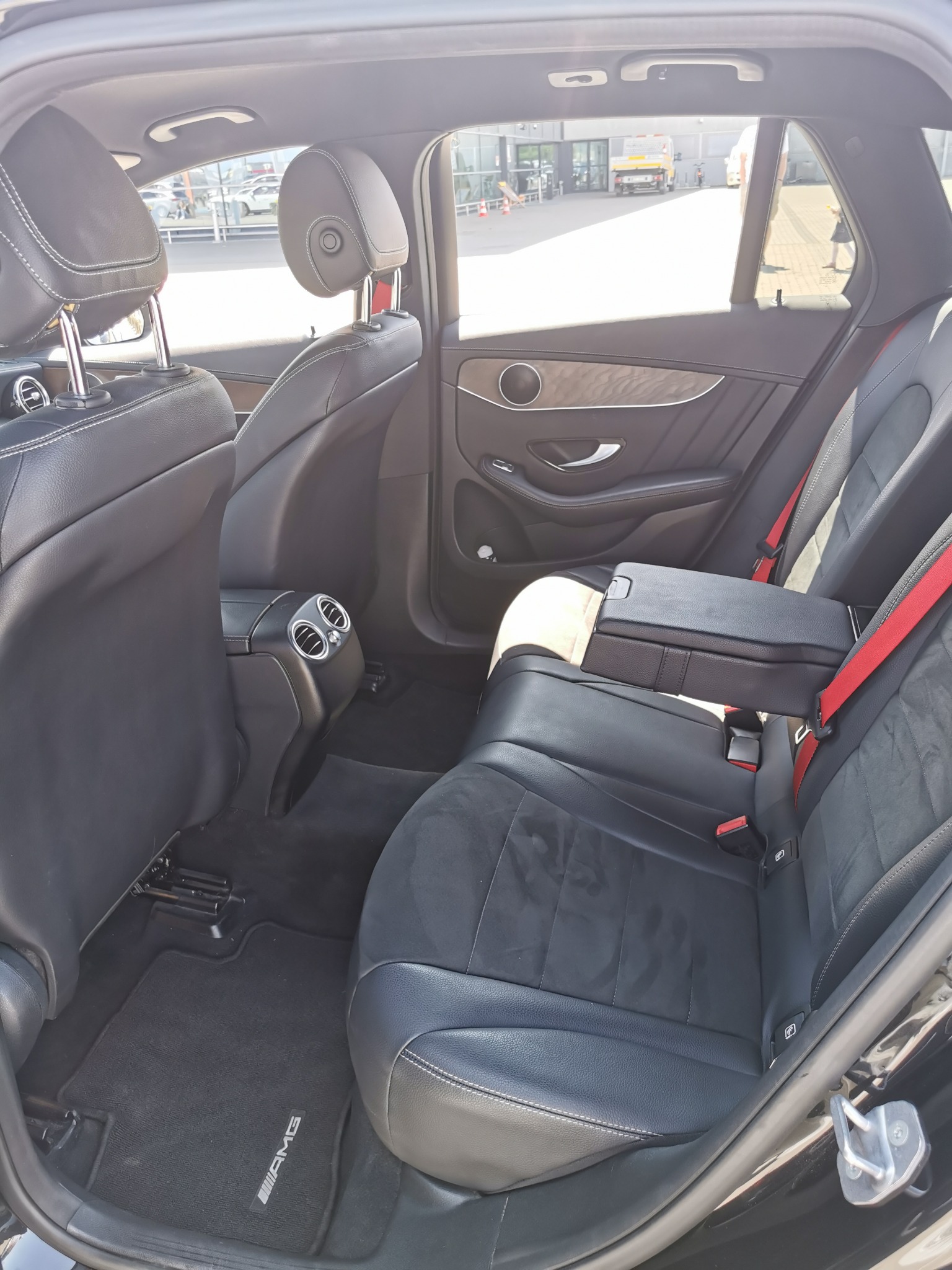 Wnętrze samochodu Mercedes GLC 220d 4matic kombi, widok na tylne siedzenia z czarnej skóry z czerwonymi pasami bezpieczeństwa i podłogą z logo AMG.