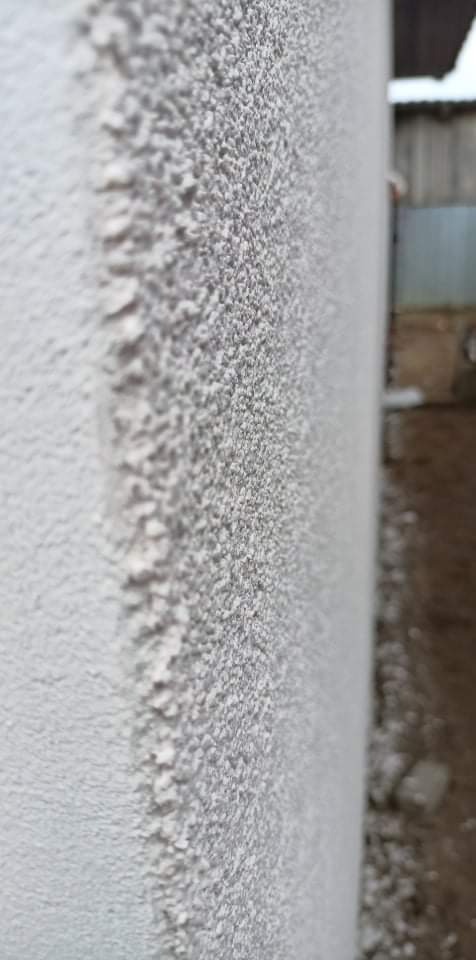 Szary tynk sylikonowo-sylikatowy o wyraźnej fakturze na elewacji budynku, widoczny z bliska z perspektywy bocznej, z fragmentem narożnika ściany