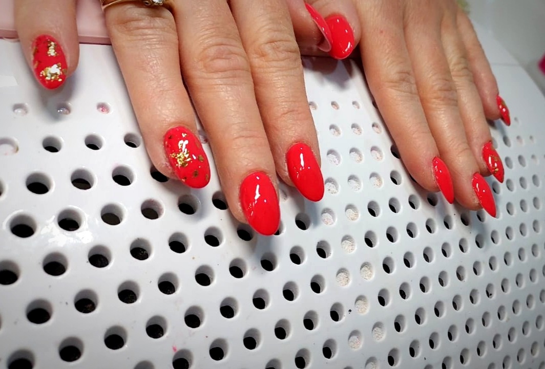 Czerwone paznokcie, niektóre ozdobione złotymi płatkami, świeżo po utwardzeniu pod lampą UV
