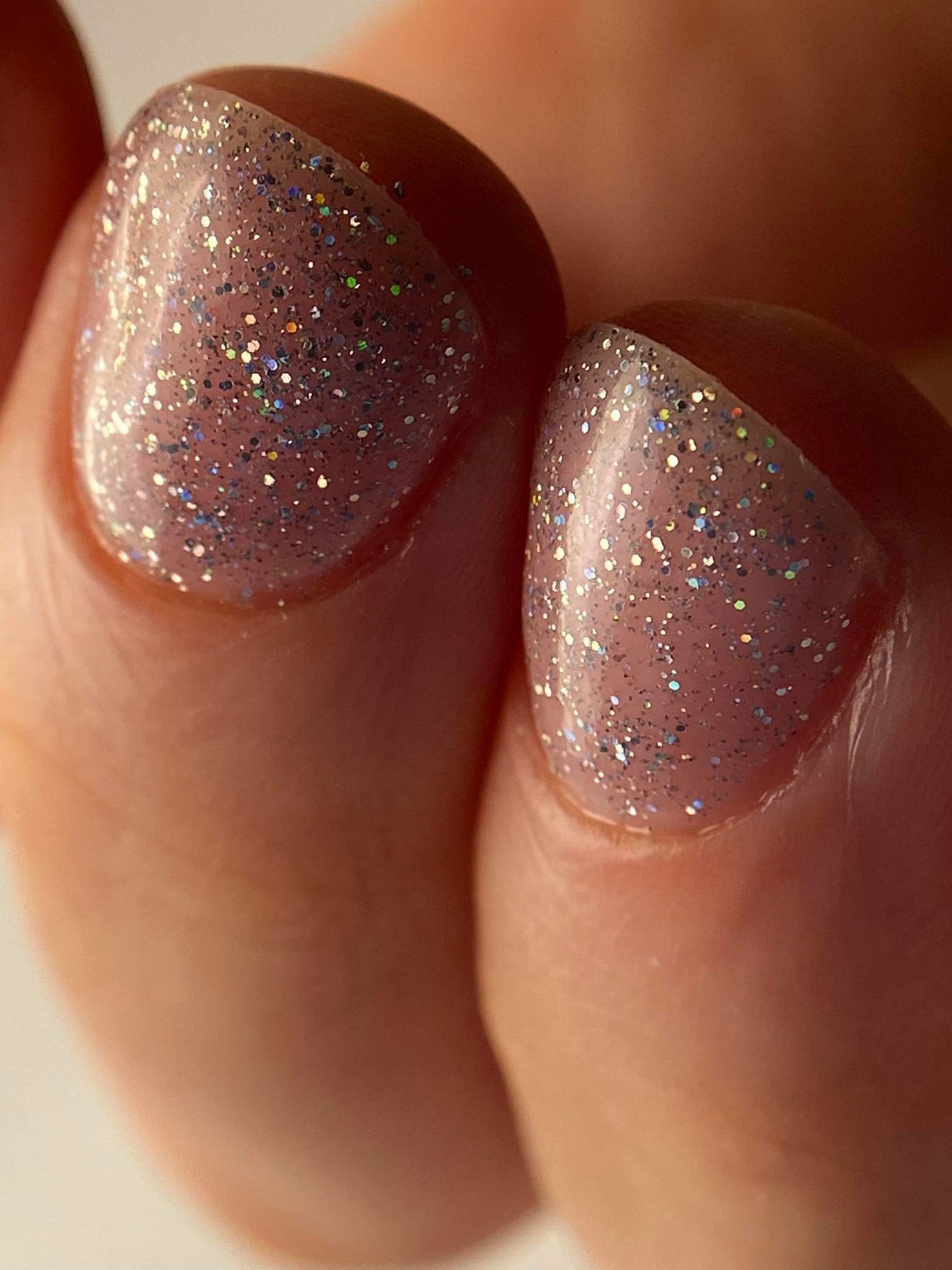 Zbliżenie na dwa palce z błyszczącym, różowym lakierem hybrydowym z efektem brokatu i holograficznymi drobinkami, precyzyjnie nałożonym na paznokcie.