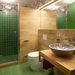 Nowoczesna łazienka z zielonymi płytkami podłogowymi i ściennymi w kabinie prysznicowej, drewnopodobnymi panelami ściennymi, wiszącą toaletą i umywalką nablatową w etniczne wzory.