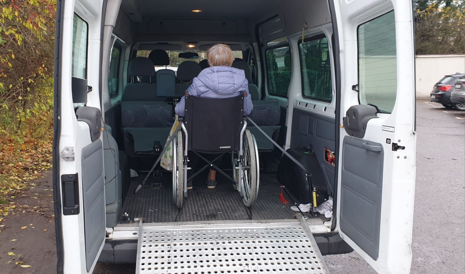 Osoba na wózku inwalidzkim zabezpieczona pasami wewnątrz białego busa z rozłożoną rampą wjazdową.