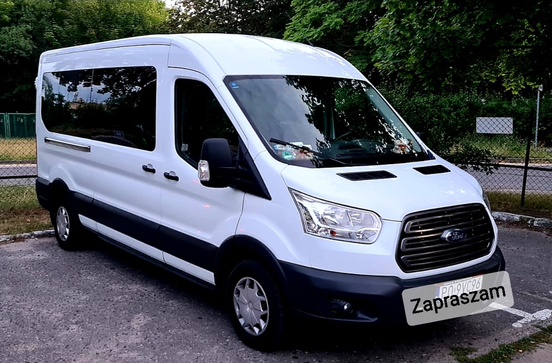 Biały bus marki Ford Transit z przyciemnianymi szybami, zaparkowany na zewnątrz, widok z przodu i boku.