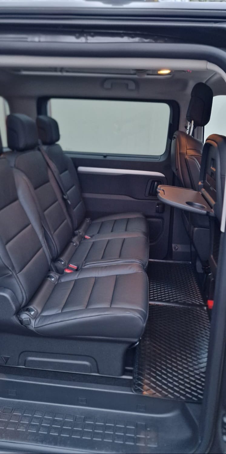 Wnętrze czarnego busa z trzema rzędami skórzanych siedzeń, widok z otwartych drzwi w Poznaniu.