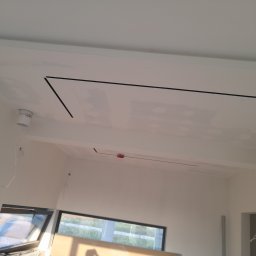 Serwis remontowy BEZ-VAS - Biały sufit z płyt kartonowo-gipsowych, widoczne czarne linie wyznaczające kształt, okno w tle. Wnętrze w trakcie wykończenia.