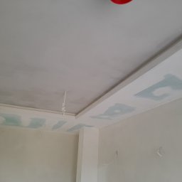 Serwis remontowy BEZ-VAS - Wnętrze w trakcie prac wykończeniowych: sufit z elementami płyty gipsowej, widoczne łączenia i szpachlowanie. Ściany w jasnym odcieniu, przygotowane do malowania.