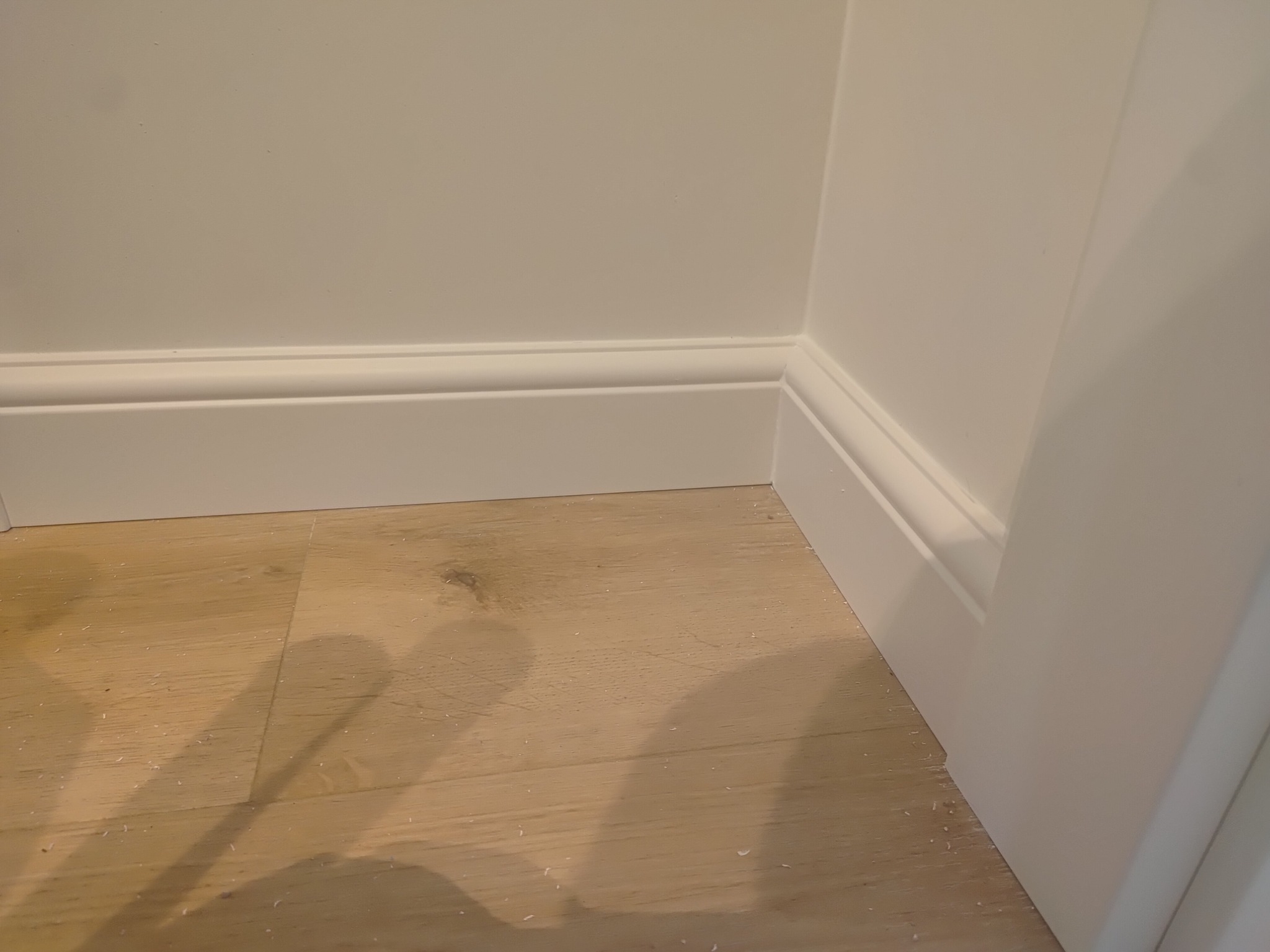 Jasne panele podłogowe i białe listwy przypodłogowe przy ścianie. Detal wykończenia wnętrza, widok z niskiej perspektywy, podkreślający precyzję wykonania.