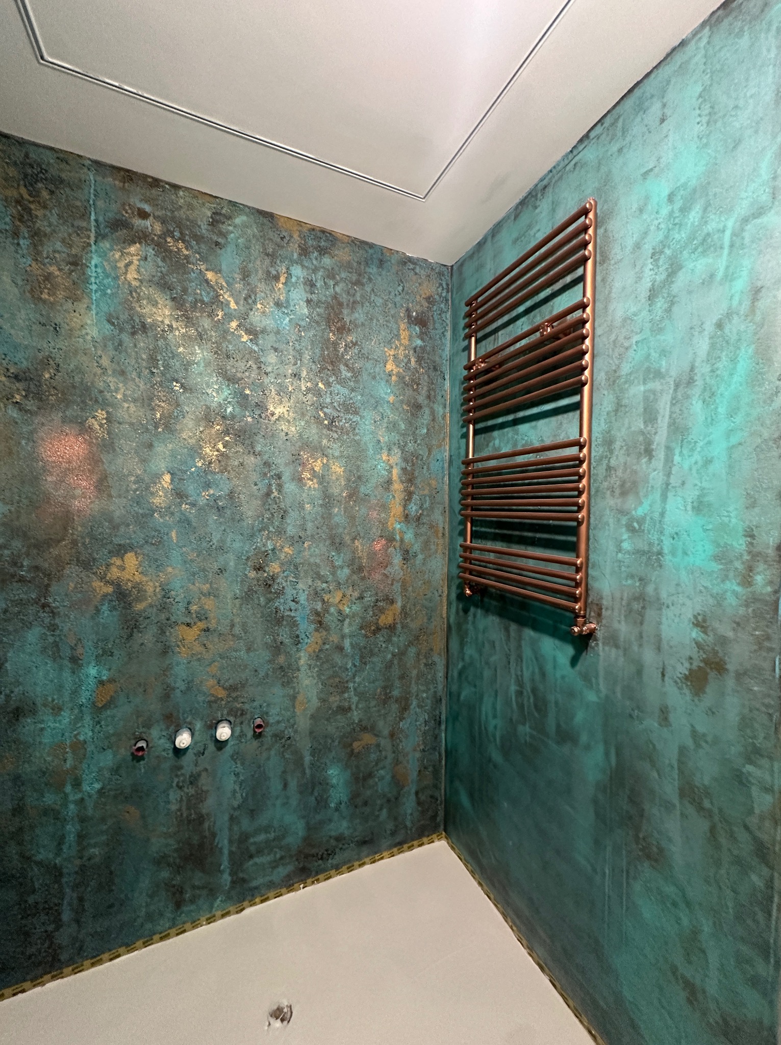 Łazienka z dekoracyjną ścianą w odcieniach turkusu i złota, miedziany grzejnik drabinkowy, przygotowane punkty oświetleniowe.