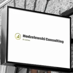Szyld reklamowy firmy Modzelewski Consulting z logo przedstawiającym wykres wzrostu w złotej obwódce, zamontowany na szarej, kamiennej ścianie budynku.