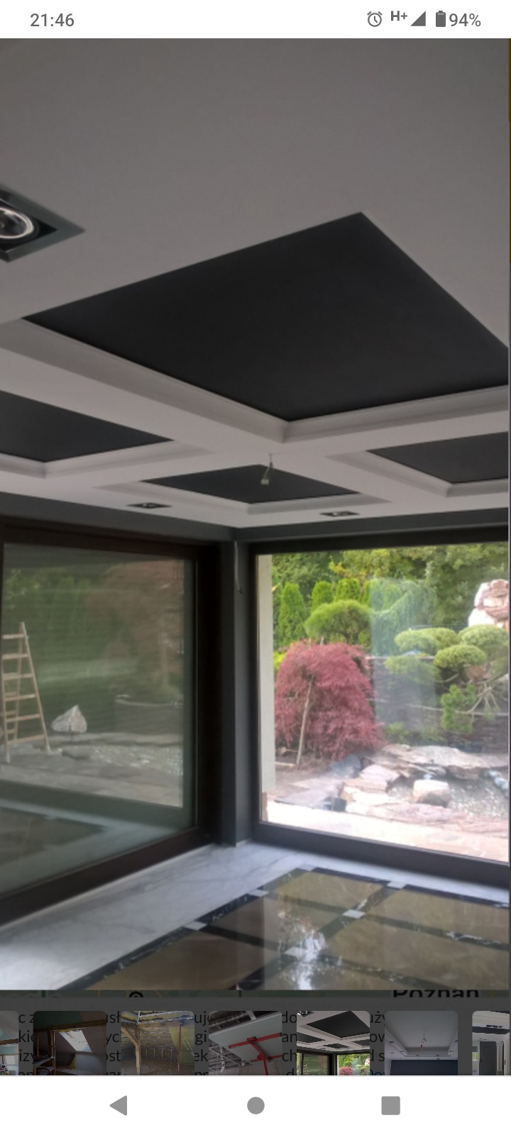 Dekoracyjny sufit z czarnymi wstawkami i białymi listwami, widok na ogród przez duże okna.