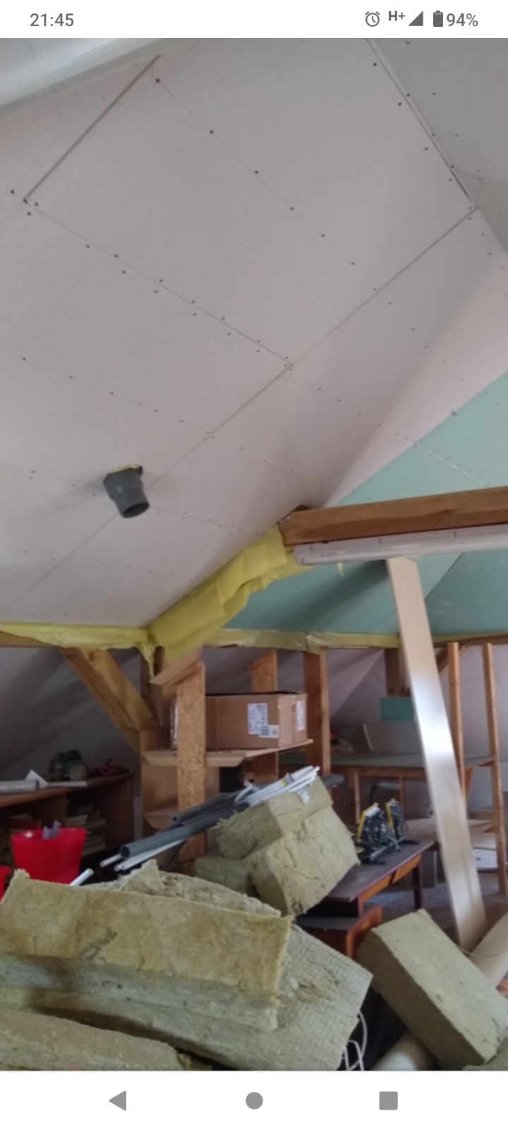 Poddasze w trakcie ocieplania i montażu płyt w Szczecinie, widoczne wełna mineralna, fragment konstrukcji drewnianej, rura wentylacyjna wystająca z sufitu, oraz częściowo zamontowane płyty.