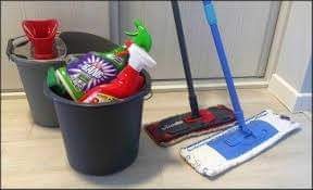 Dwa wiadra: jedno puste z czerwonym wkładem, drugie wypełnione środkami czystości, obok dwa mopy stojące oparte o białe drzwi.