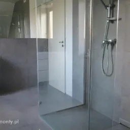 Nowoczesna łazienka z kabiną prysznicową typu walk-in, szare płytki wielkoformatowe, biała szafka pod umywalką z szufladami, minimalistyczna armatura.