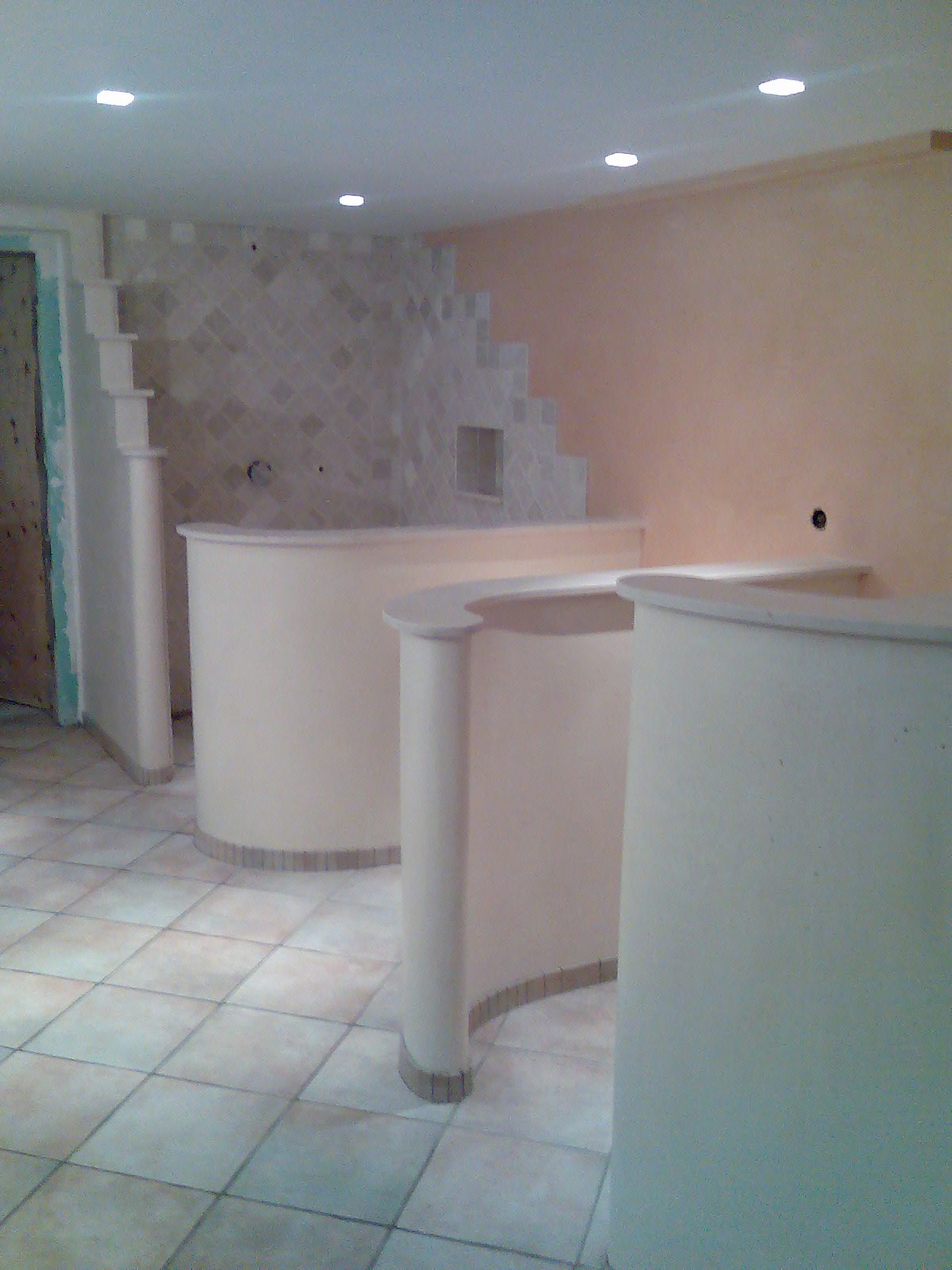 Niedokończona łazienka z zaokrąglonymi ściankami działowymi, mozaiką na ścianie i niedokończonymi drzwiami.