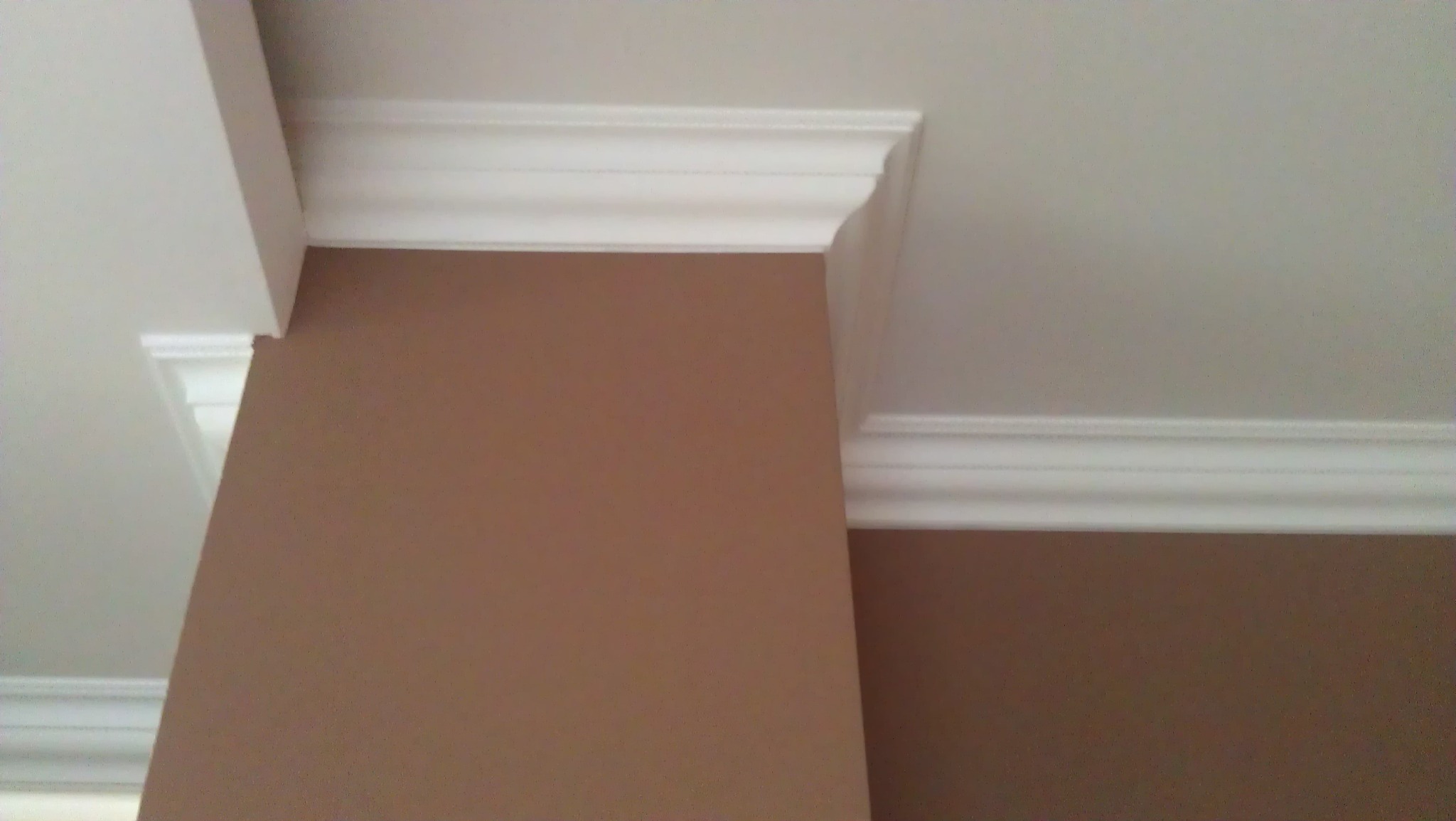 Brązowa ściana z białym, ozdobnym gzymsem i listwami przysufitowymi, widok z dołu.