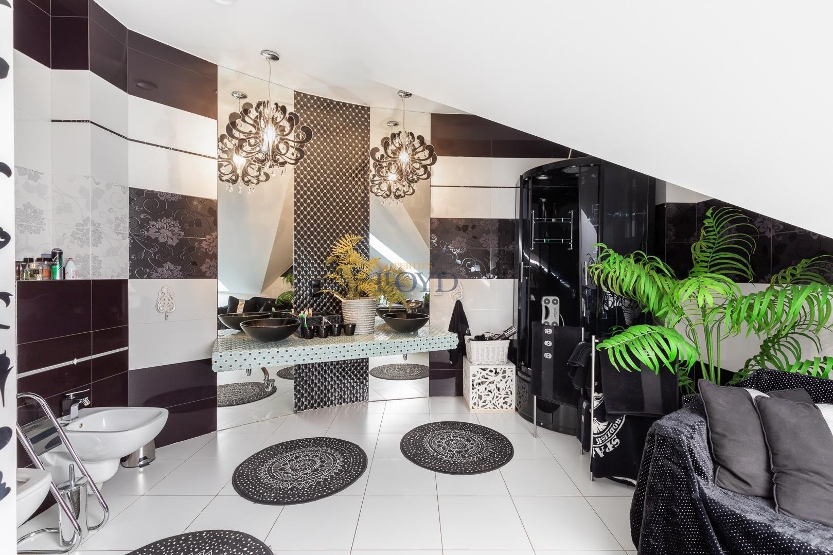 Elegancka łazienka w czarno-białej kolorystyce z dwoma umywalkami w kształcie mis, lustrem na całą ścianę, kabiną prysznicową i rośliną doniczkową, oświetlona przez ozdobne żyrandole.