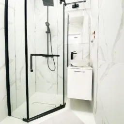 Nowoczesna łazienka z kabiną prysznicową typu walk-in z czarnymi profilami, białą umywalką nablatową i marmurowymi płytkami na ścianach.