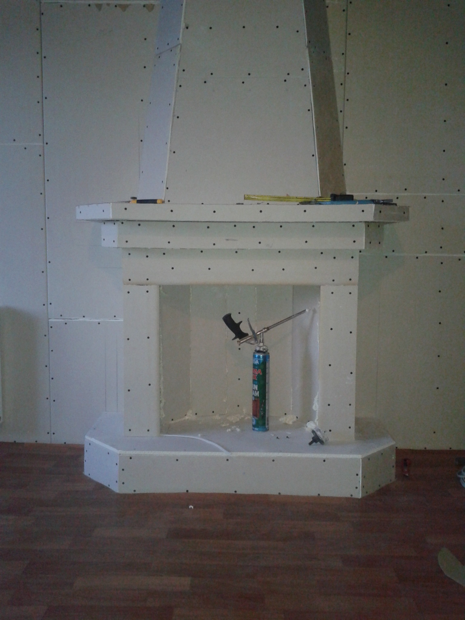 Konstrukcja kominka z płyt gipsowo-kartonowych w trakcie montażu, z widoczną pianką montażową i narzędziami, na tle ścian wykończonych płytami g-k.