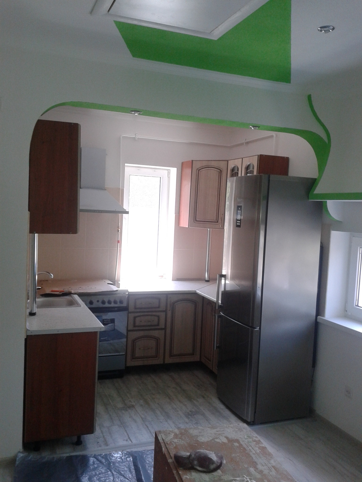 Kuchnia po remoncie z zielonymi akcentami: pomalowany sufit i łuk nad przejściem, widoczne meble kuchenne, sprzęt AGD i podłoga wyłożona panelami.