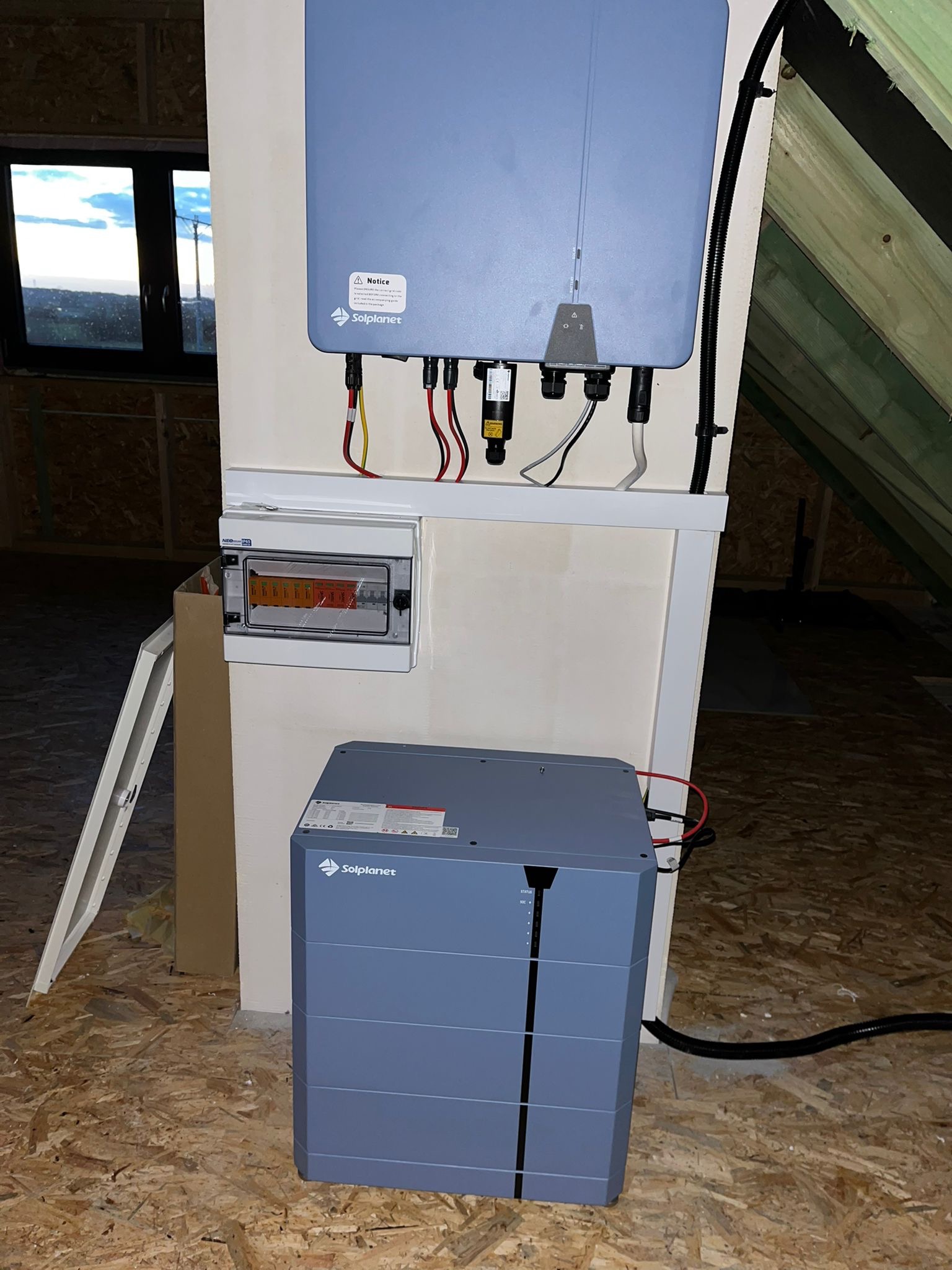 Instalacja magazynu energii Solplanet w surowym pomieszczeniu poddasza, widoczny rozdzielacz elektryczny i okno dachowe.