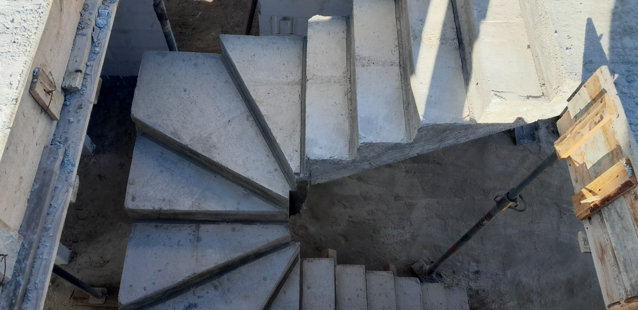 Betonowe schody spiralne w trakcie budowy, widok z góry, szalunki drewniane po bokach, podpory metalowe, surowy stan.