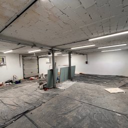 atcc z.o.o - Przestronne pomieszczenie w trakcie remontu, zabezpieczone folią malarską, widoczne instalacje elektryczne pod sufitem, przygotowane płyty gipsowo-kartonowe i materiały malarskie.