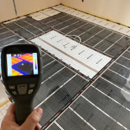 Pomiar temperatury maty grzewczej w podłodze za pomocą kamery termowizyjnej, widoczny rozkład temperatur na ekranie urządzenia.